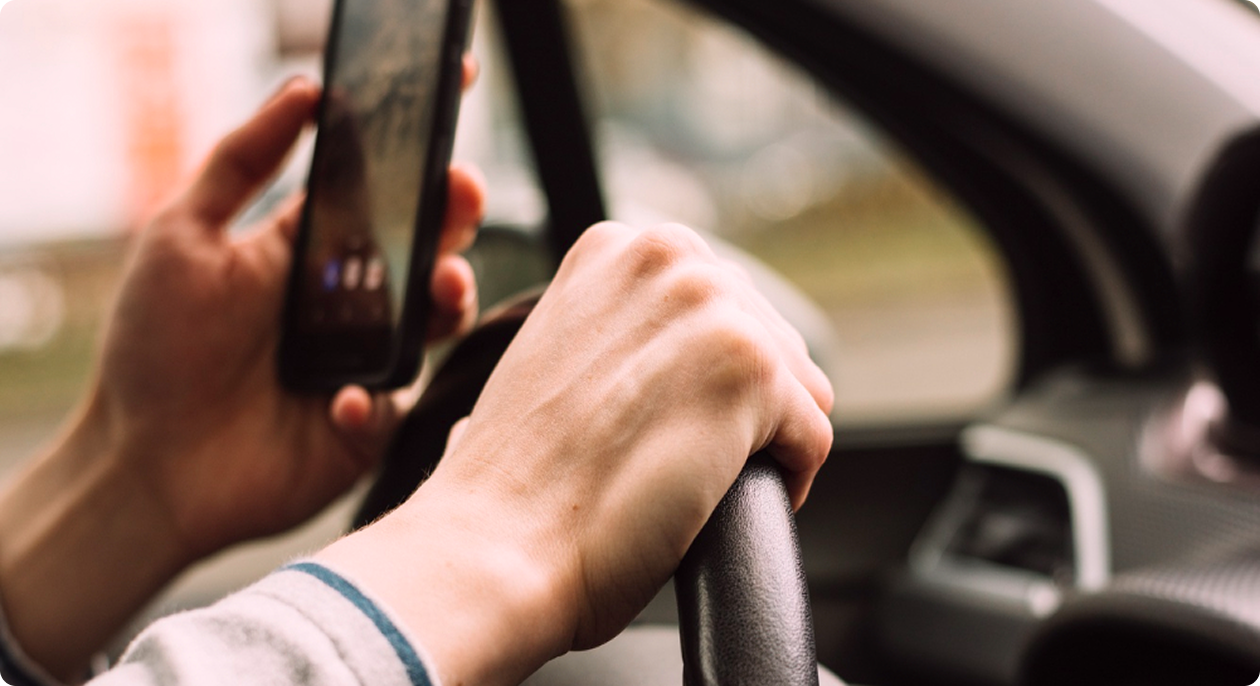 Hands on a steering wheel while holding a smartphone