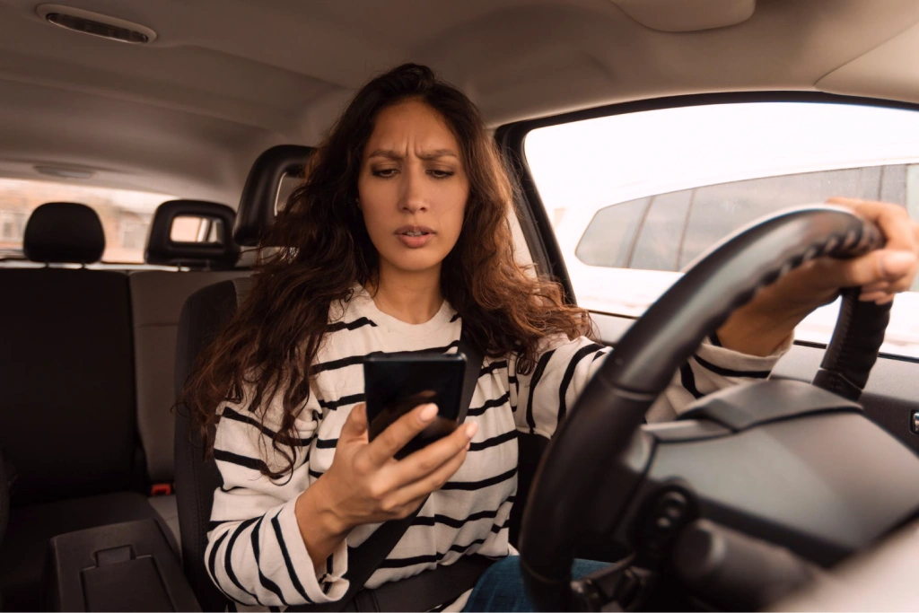 Driver looking at a smartphone while holding the steering wheel