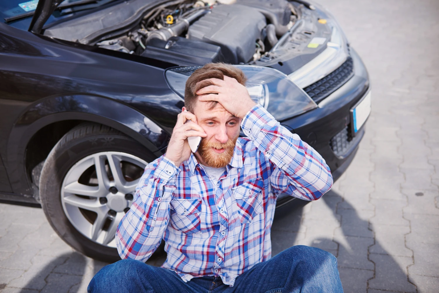 Driver sitting beside a wrecked car while calling for help